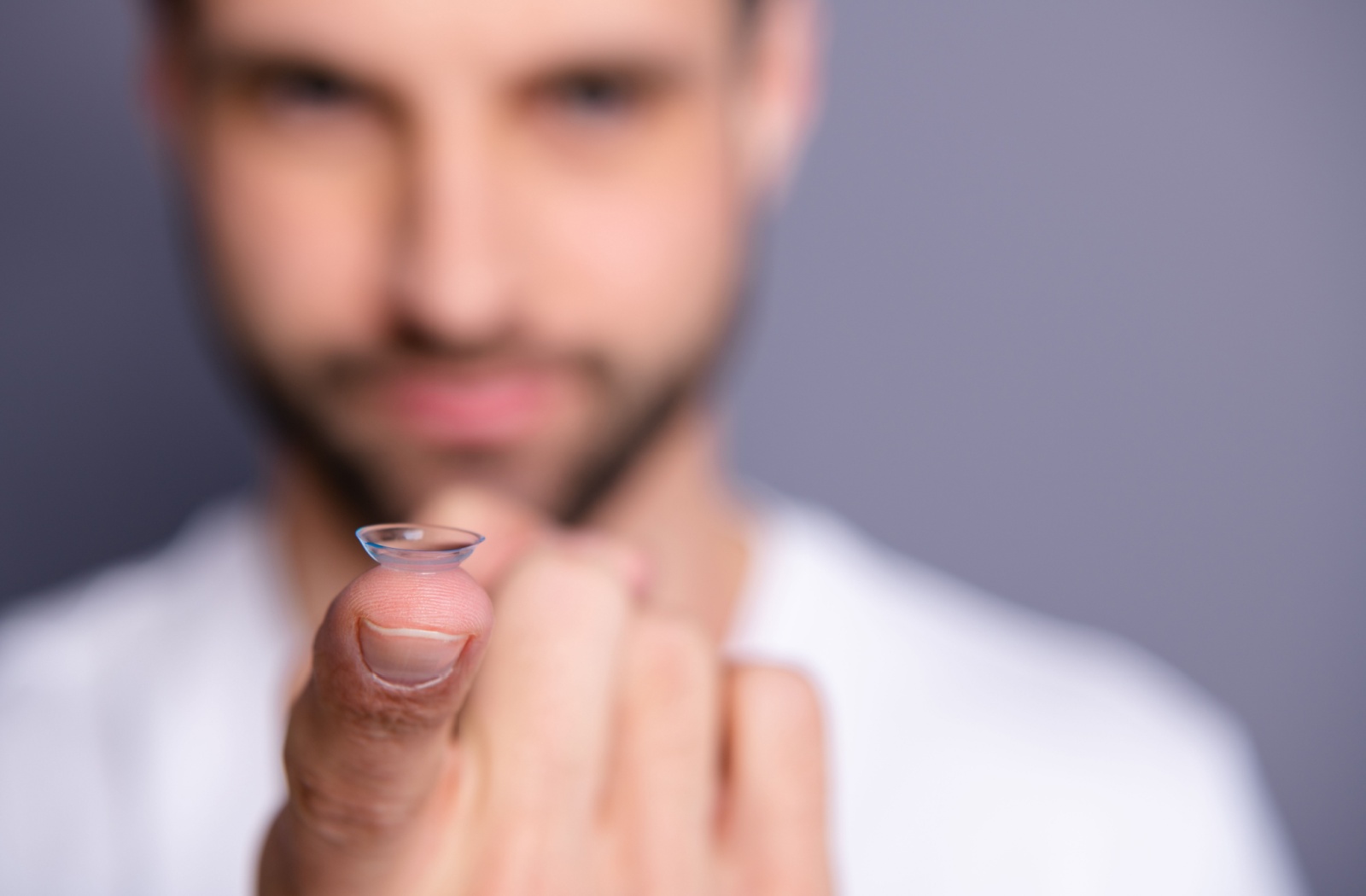 An out-of-focus person extends a finger with a contact lens resting ontop