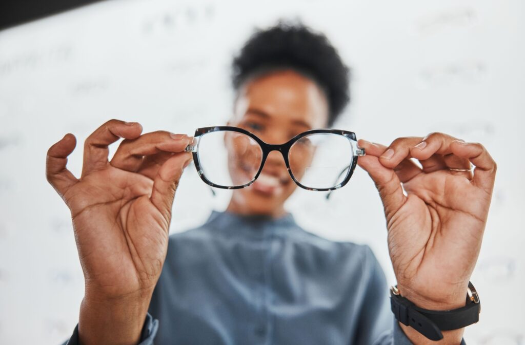 An optometrist holding up a pair of glasses, as if fitting them to someone off camera.