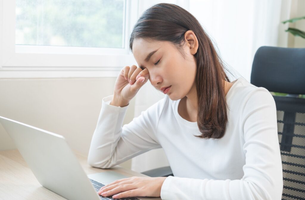 A person working on a computer rubs their eye while wearing contact lenses.