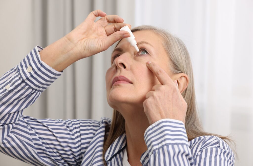 A person tilts their head back and pulls down their lower eyelid to apply artificial tears.