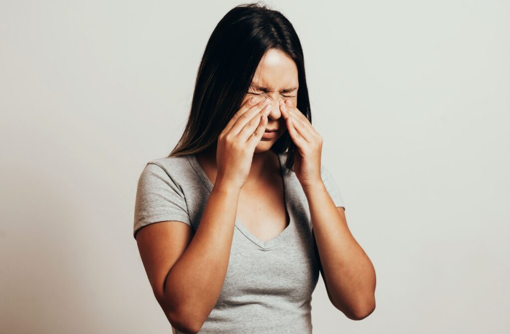 An adult pinches the bridge of their nose as they experience sinus discomfort.