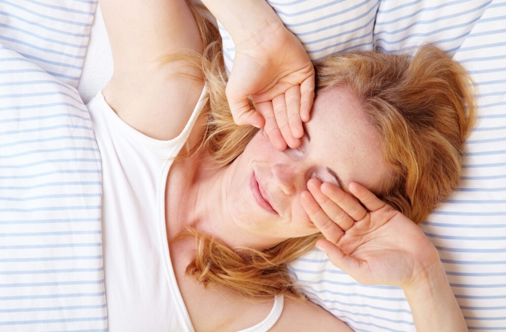 A birds-eye view of a person waking up in their bed, rubbing their eyes due to blurry vision in the morning.