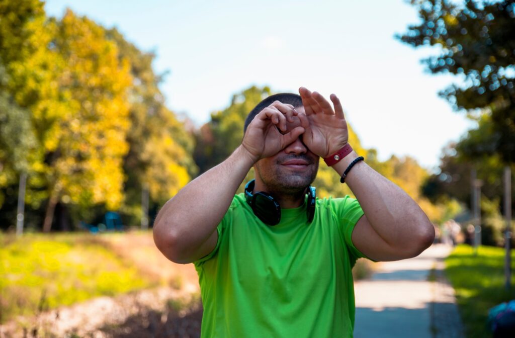 A person outside, rubbing their eyes due to irritation caused by allergens in the environment.
