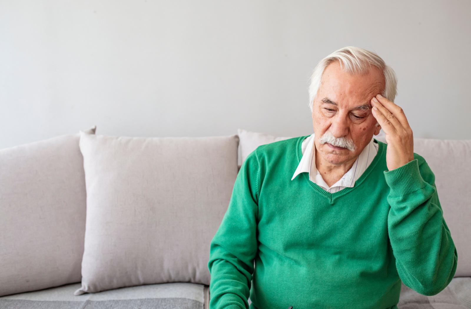 A person sitting on a couch, holding their head, experiencing dizziness symptoms of vertigo.